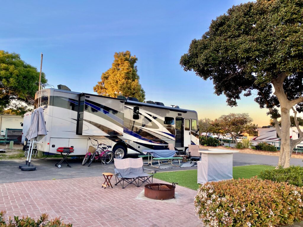 RV in a camping space with fire ring, chair bikes and barbecue for grilling.